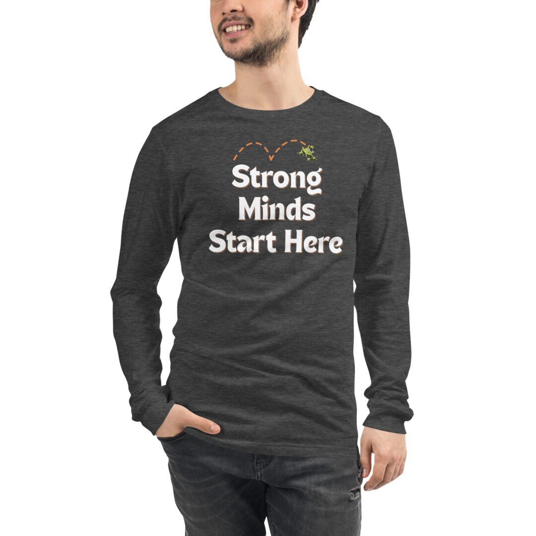 "Strong Minds Start Here" Unisex Long Sleeve Tee (Positive Leaps logo on back) 9 A person wearing a charcoal heather long-sleeved shirt with the encouraging message, "Strong Minds Start Here," and a small frog graphic.