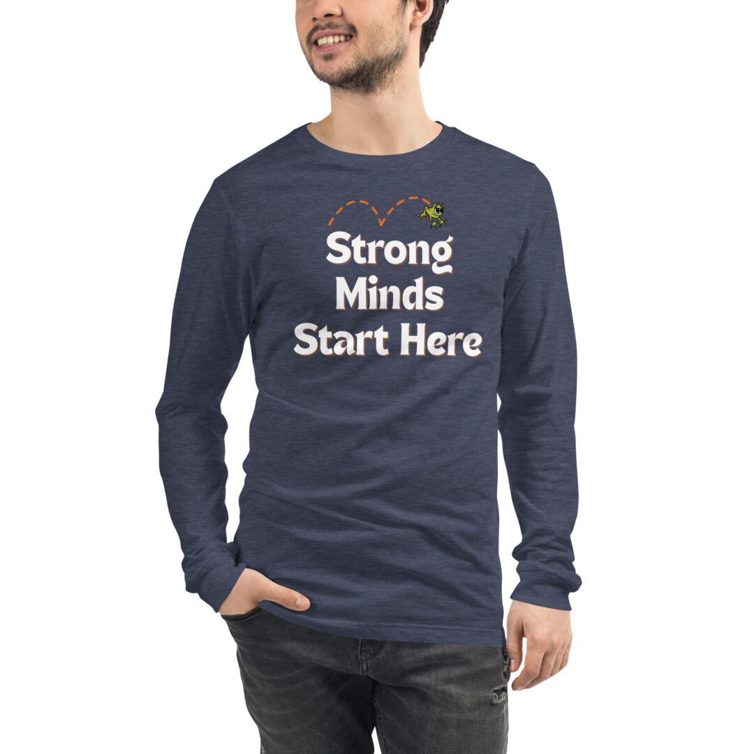 "Strong Minds Start Here" Unisex Long Sleeve Tee (Positive Leaps logo on back) 13 A person models a navy heather long-sleeved shirt with the encouraging message, "Strong Minds Start Here," and a small frog graphic.